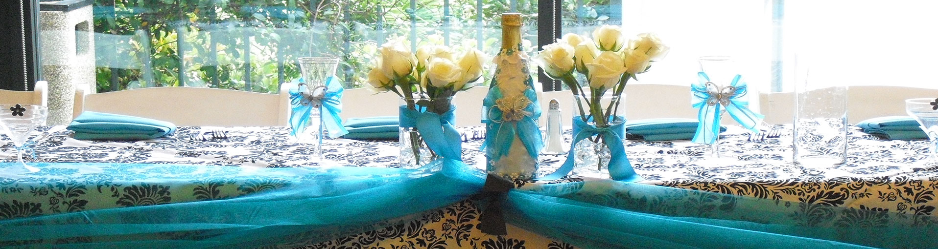 Table with white tablecloth and blue designs holding champagne bottle and roses in a quinceanera event venue in Las Vegas and Henderson NV.